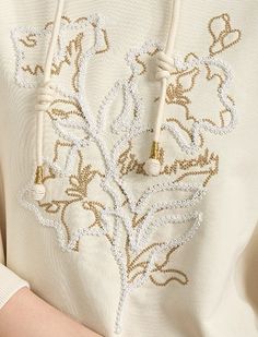 a close up of a person wearing a white shirt with gold threadwork on it