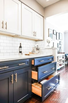 an open drawer in the middle of a kitchen with white cabinets and blue drawers on both sides