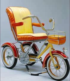 an orange and yellow bike with a basket attached to the front wheel, sitting on a white surface