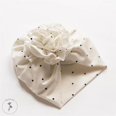 a white and black polka dot hair bow on top of a white cloth napkin with a flower in the center