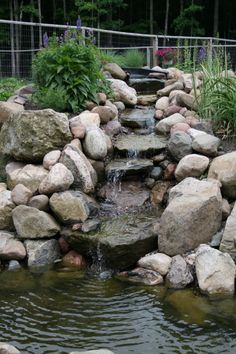 there is a small pond with rocks and water running down the sides, surrounded by greenery