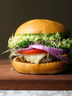 a hamburger with lettuce, tomato, and onion on it sitting on top of a wooden table