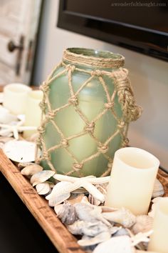 a green vase sitting on top of a wooden tray next to candles and seashells