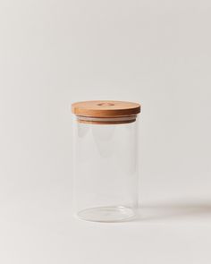 a glass jar with a wooden lid on a white surface, against a plain background