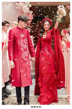 a man and woman dressed in traditional chinese garb holding hands as confetti falls from the sky