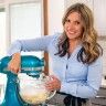 a woman is standing in front of a mixer and mixing something with her hands, smiling at the camera