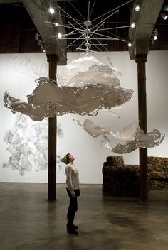 a woman is standing in an art gallery looking up at a sculpture hanging from the ceiling