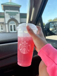 a person holding up a pink drink in their hand while sitting in the back seat of a car