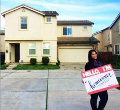 a woman standing in front of a house holding a sign