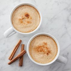 two cups of coffee with cinnamon sticks next to them