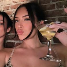 two beautiful women standing next to each other holding drinks in front of their faces and posing for the camera