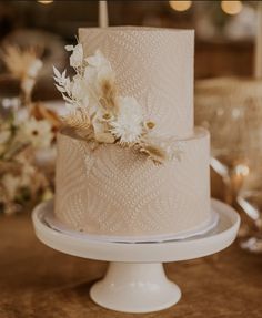 a three tiered wedding cake with white flowers on the top and gold leaf decoration