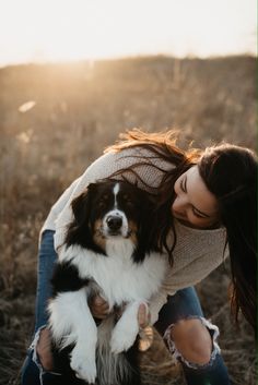 a woman kneeling down holding a dog in her lap with the sun shining on her