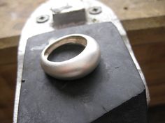 a metal object sitting on top of a piece of black wood with a ring in the middle