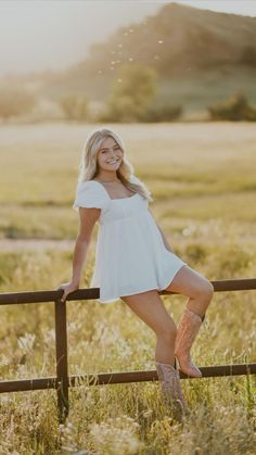 a beautiful blonde woman leaning on a fence posing for the camera with her legs crossed