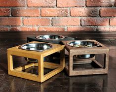 three wooden dog bowls with their lids open on the floor in front of a brick wall