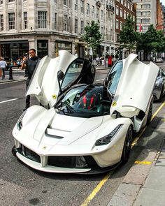 two white sports cars parked next to each other on the side of the road with open doors