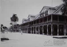 an old black and white photo of a building with palm trees on the street in front of it