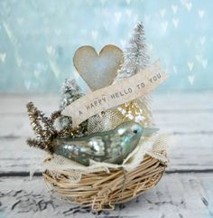 a bird sitting on top of a nest filled with christmas decorations and a ribbon that says happy hello to you