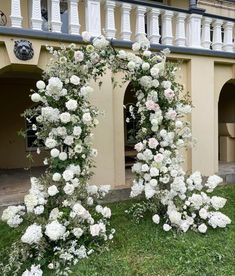 an outdoor wedding arch with white flowers and greenery in front of a house on the lawn