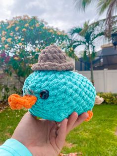 a hand holding a crocheted blue bird with an orange beak and hat on it's head