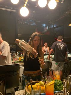 a woman standing in front of a counter filled with fruit and drinks while holding a blender