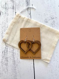 two wooden heart shaped earrings sitting on top of a piece of paper next to a bag