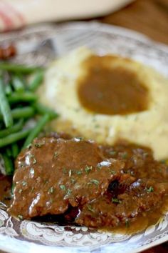 a plate topped with meat and gravy next to green beans