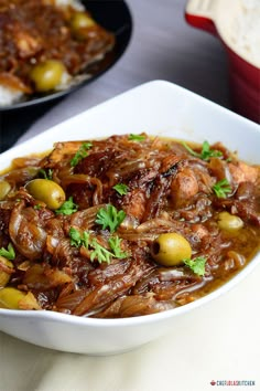 a white bowl filled with meat and olives