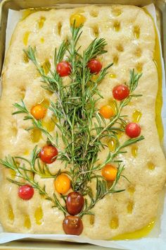 an uncooked pizza with tomatoes, olives and rosemary sprigs on top