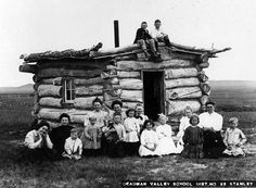 black and white photograph of people sitting on the roof of a log cabin with logs