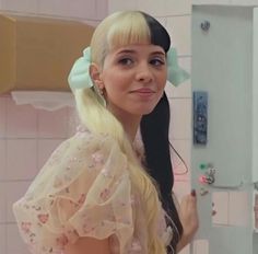 a woman with long blonde hair wearing a pink dress and green bow in front of a mirror