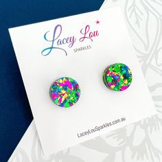 pair of colorful earrings on card with blue background and white flowered paper in the foreground