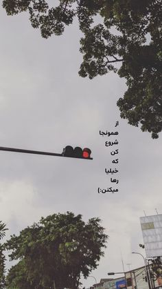 a traffic light with arabic writing on the side and trees in the backgroud