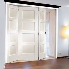 an empty room with white doors and hard wood flooring on the side, in front of a lamp