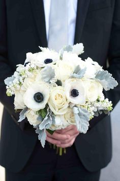 a man in a suit holding a bouquet of white and black flowers on his lapel