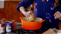 a woman is pouring something into an orange pot on the stove top with other cans nearby