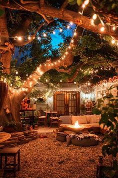 an outdoor seating area with lights strung from the trees and on the ground, in front of a house