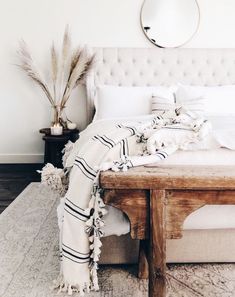 a bed with white linens and pillows on it, next to a wooden table