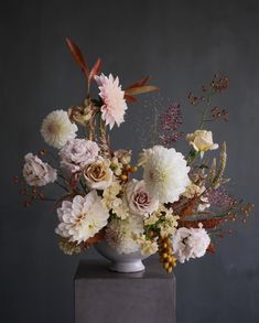 a white vase filled with lots of flowers on top of a wooden table next to a gray wall