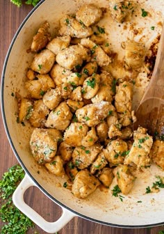 chicken and parsley in a skillet with a wooden spoon