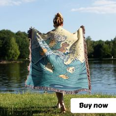 a woman is holding up a blanket in front of the water