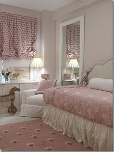 a bedroom with pink and white bedding, window curtains, rugs and furniture