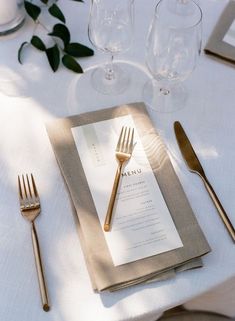 a place setting with silverware and napkins on a white table cloth, surrounded by greenery