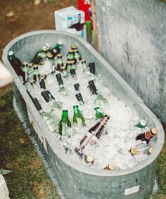 a tub filled with lots of bottles of beer sitting on top of a grass covered field