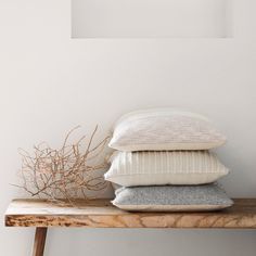 three pillows stacked on top of each other on a wooden shelf next to a plant