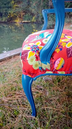 an upholstered chair sitting in the grass near a body of water and trees