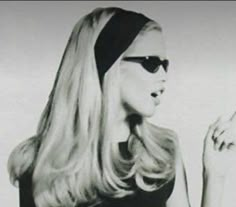 black and white photograph of a woman with long blonde hair pointing to the side while wearing sunglasses