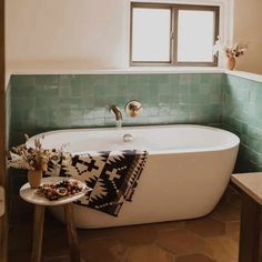 a bath tub sitting next to a window in a bathroom with green tile on the walls