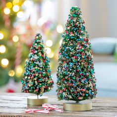 two small christmas trees sitting on top of a wooden table